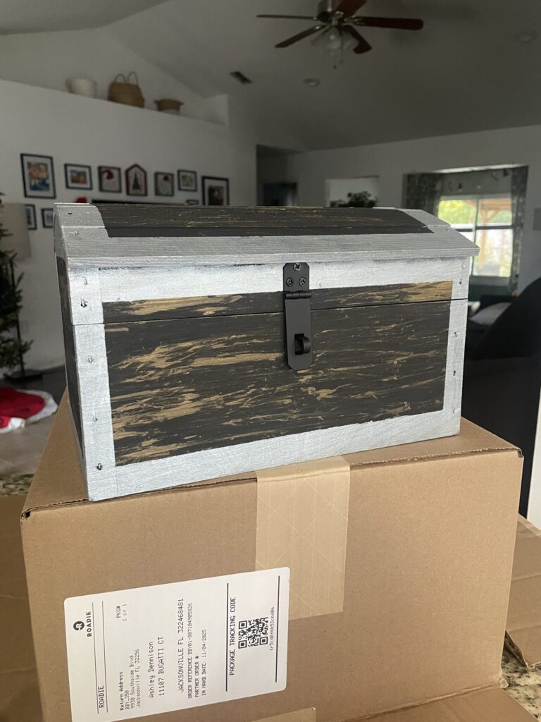 A freshly painted treasure chest sits on top of a box with drying silver paint on the edges to look like hinges holding it together.