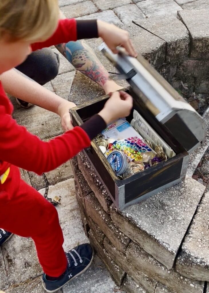 J opening his found treasure to see all the goodies that were inside, including pretend coins and gems, crafts, slime, and chocolate.