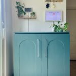 Blue-green cabinet, 3 feet high with arched cabinet doors, sitting on a wood base 3 inches off the ground