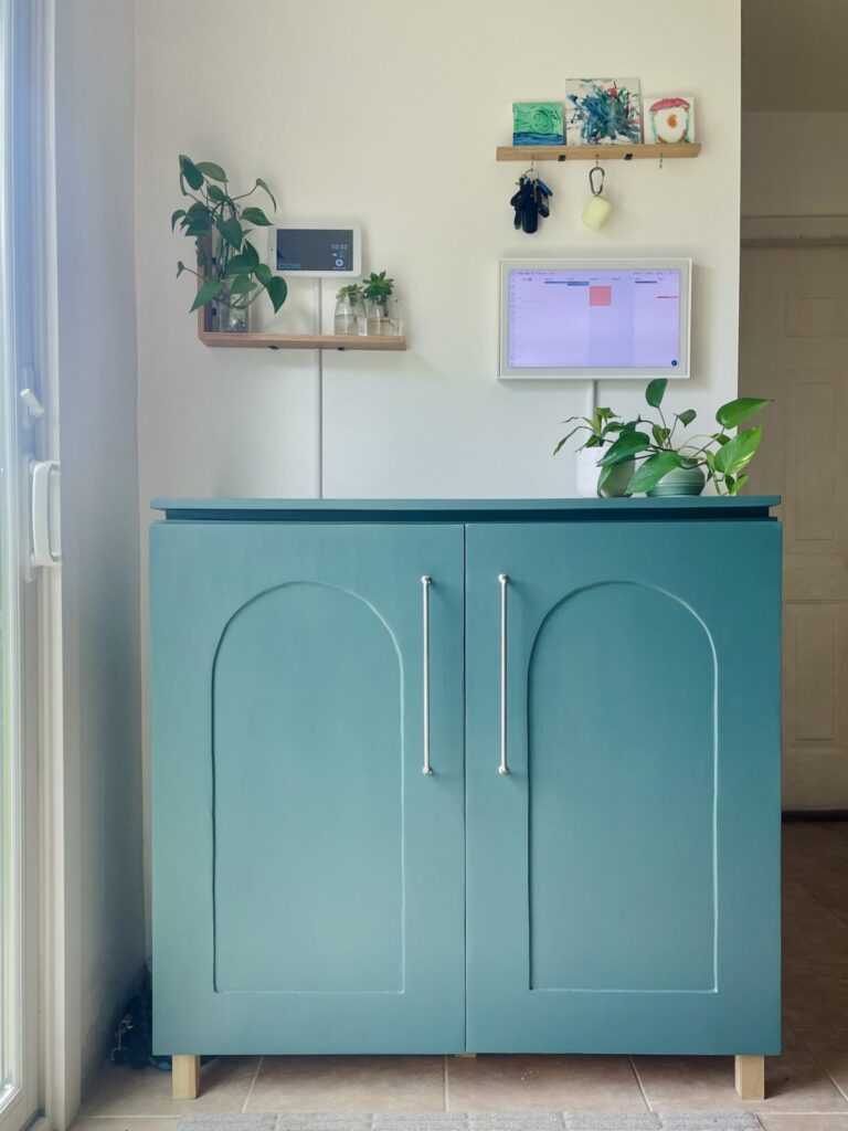 Blue-green cabinet, 3 feet high with arched cabinet doors, sitting on a wood base 3 inches off the ground